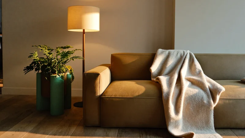Gemütliche Wohnzimmerecke mit Sofa, Stehlampe, Wolldecke und Pflanze am Abend